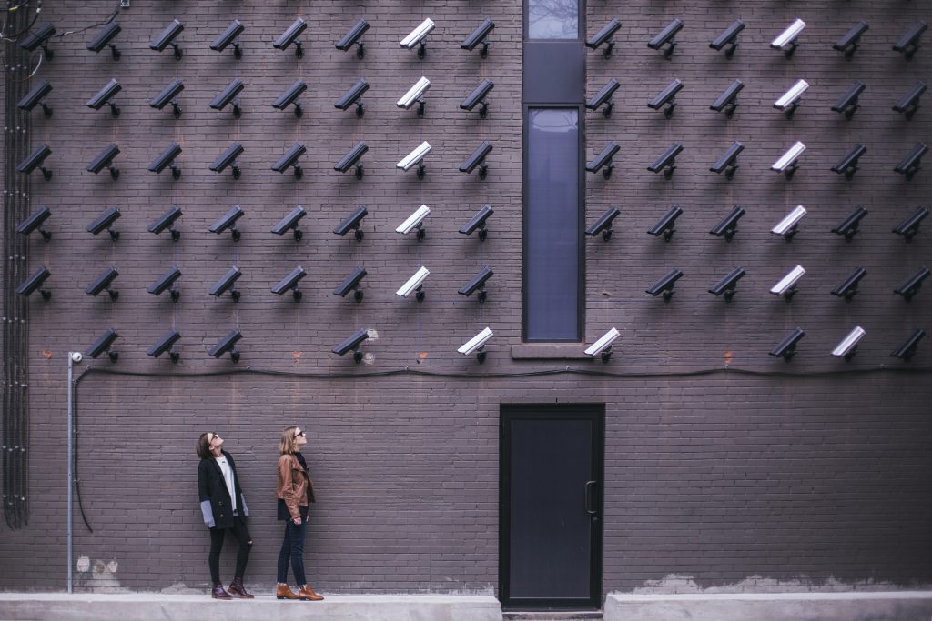Two people being watched by a wall of security cameras