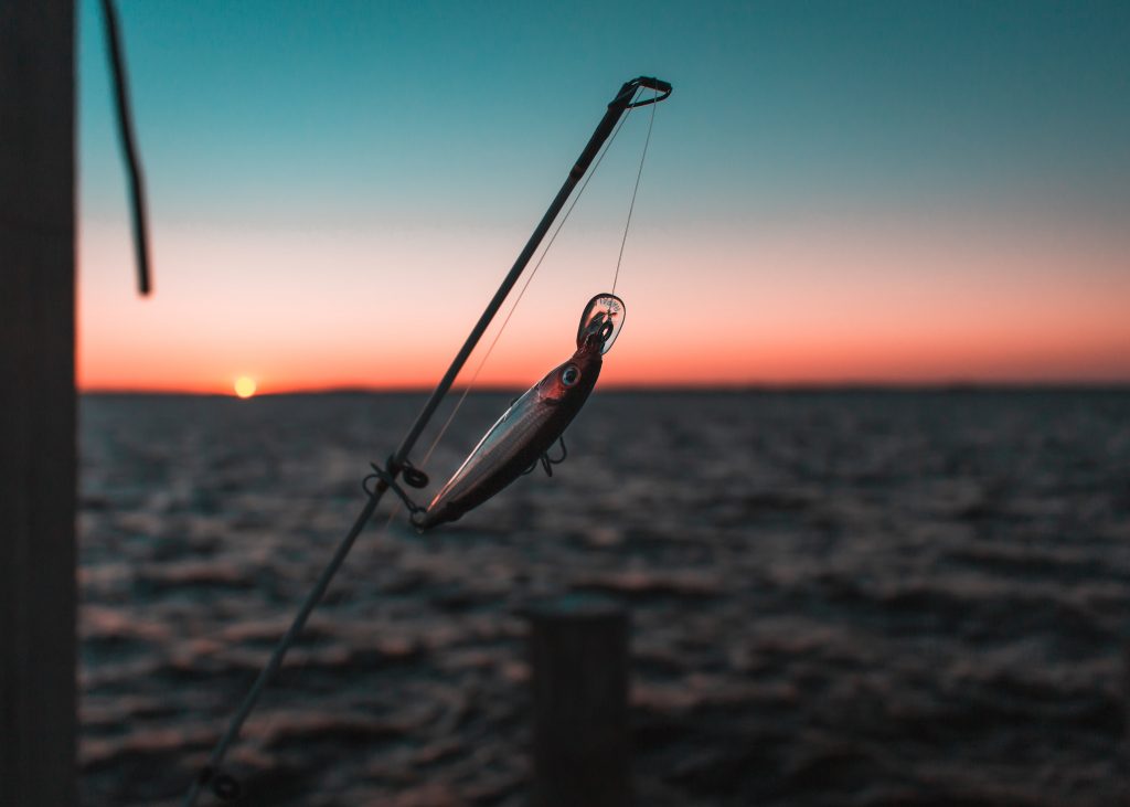 A lure on the end of a fishing rod hanging over the ocean at sunset